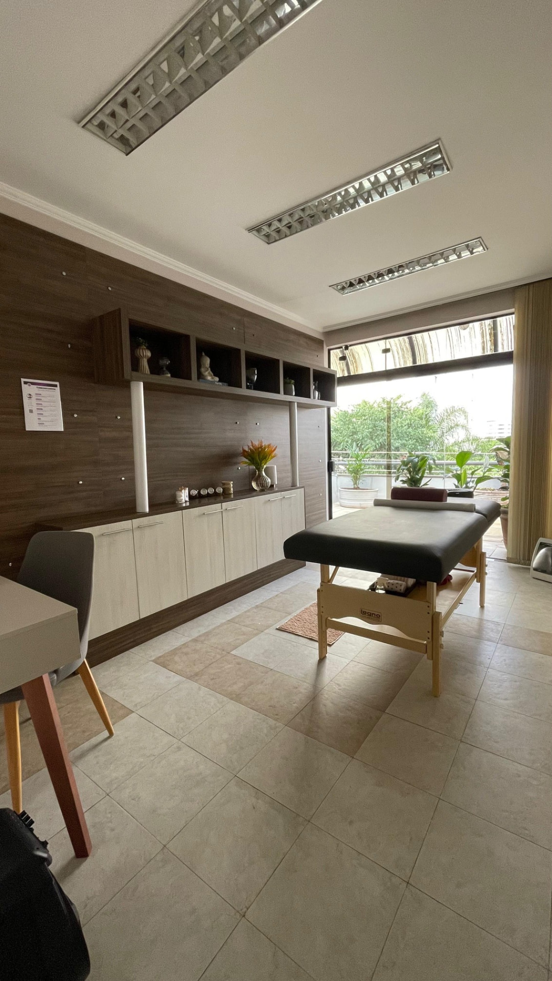 Sala de bem-estar com maca de massagem, marcenaria de madeira e varanda com plantas