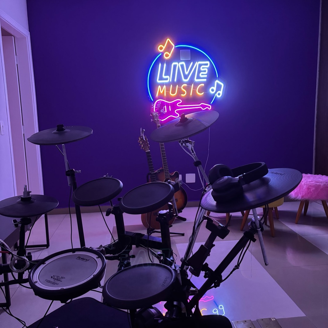 Sala de música com neon 'Live Music', bateria eletrônica Roland e violões