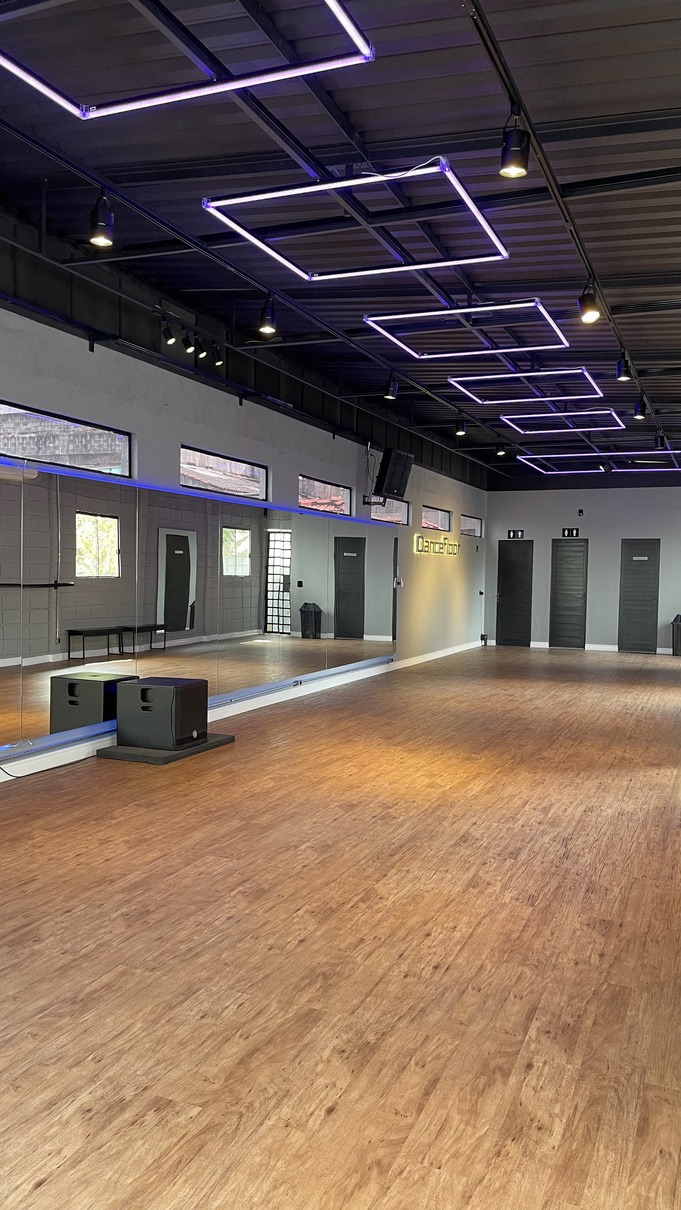 Salão do Dancefloor com piso de madeira, espelhos e luzes neon roxas no teto