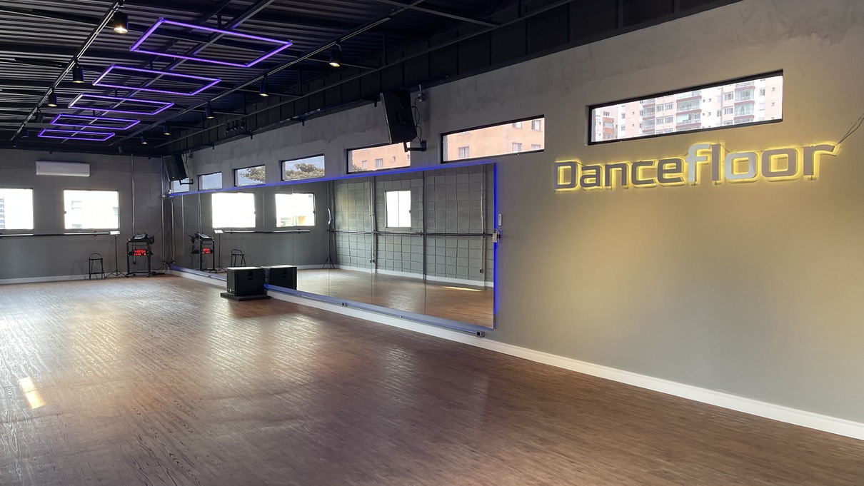 Salão de 100 m² do Dancefloor com piso de madeira, espelhos e luzes de teto em neon roxo