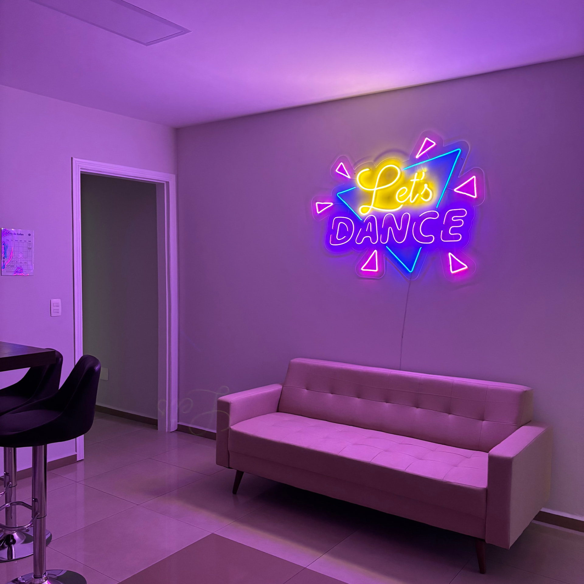 Sala de recepção do Dancefloor com sofá claro e neon colorido 'Let's Dance' na parede